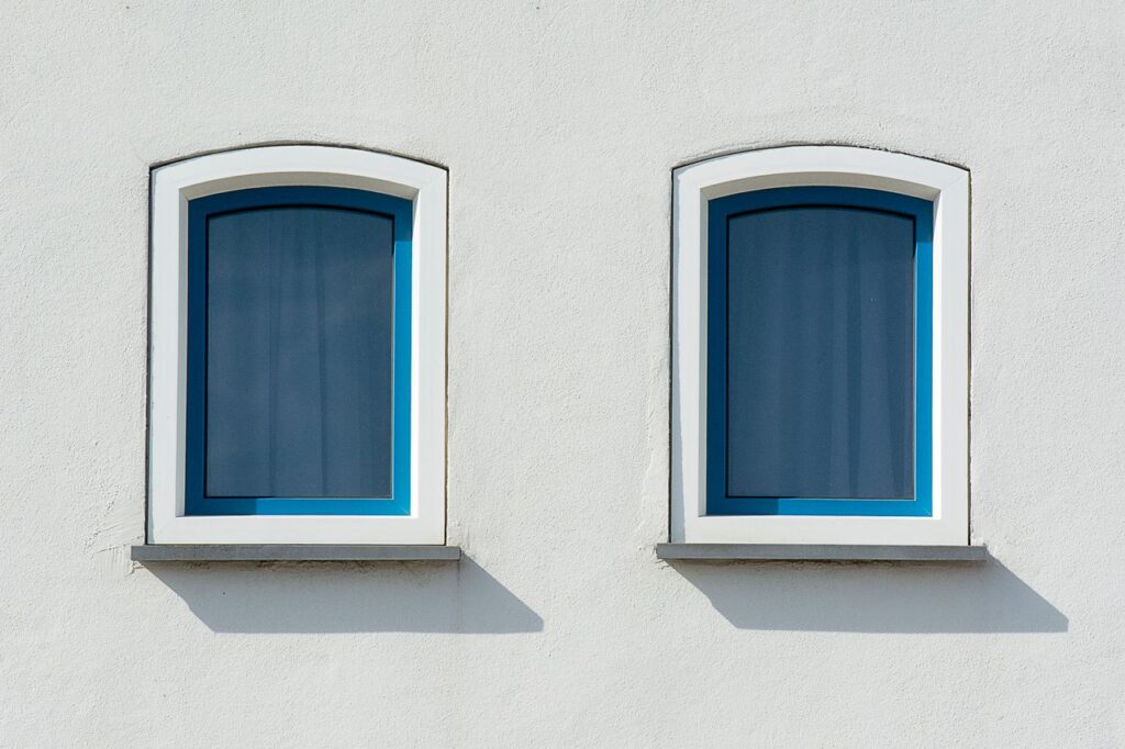A minimalist image of a white building facade featuring two blue arched windows casting shadows.