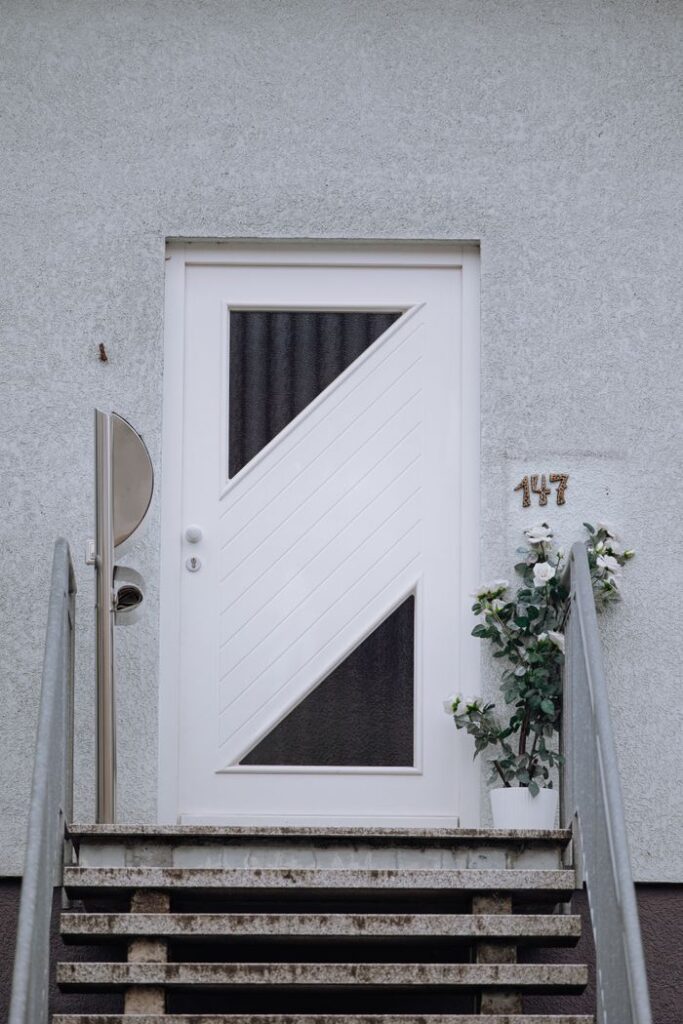 Contemporary white door with geometric design and plant accents on a staircase, showcasing urban architecture.
