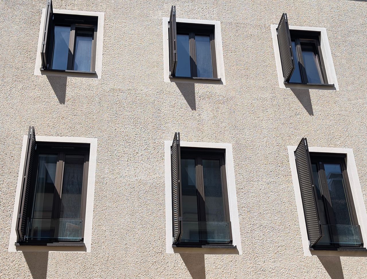 Close-up of building facade featuring open windows casting shadows, modern urban architecture.